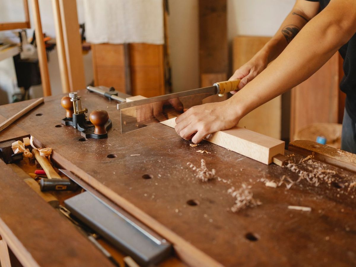 A carpenter working a timber section by hand at a bench