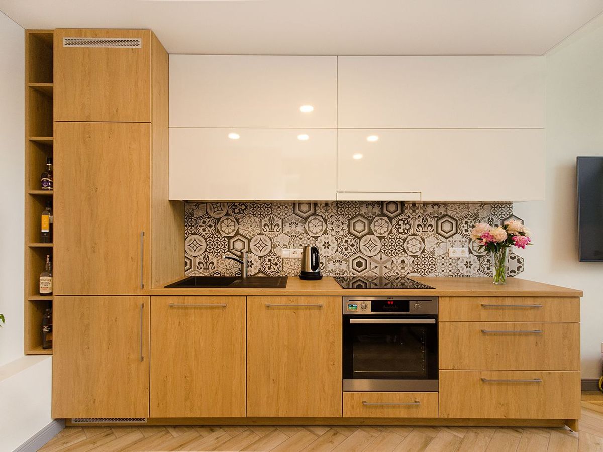 A modular kitchen in a warm wood finish, with a patterned tile splashback